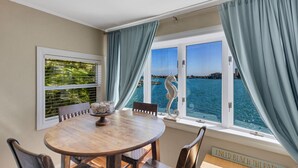 A dining area with a round table, chairs, and a view of the sea through large windows. - 🌴 Bayview Beauty @ Coral Resort | Waterfront • Pool • Dock • Walk to Beach ➠ CR B5 (Clearwater Beach)