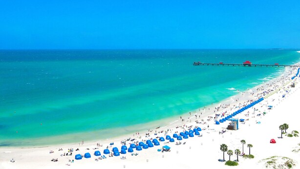 A beach with a pier extending into the ocean, numerous umbrellas, and people enjoying the beach. - 🌴 Bayview Beauty @ Coral Resort | Waterfront • Pool • Dock • Walk to Beach ➠ CR B5 (Clearwater Beach)