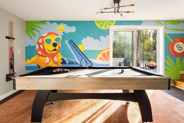 A pool table with a colorful mural, a billiards rack, and a view of the outdoors. - Sunny Spring Escape – Downtown 9 Min – Pool Tab – Relax N Raleigh (Raleigh)