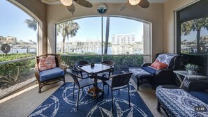 Een zonnedek met uitzicht op een jachthaven, ingericht met rieten stoelen en een tafel, en twee plafondventilatoren.