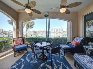 A sunroom with a view of a marina, furnished with wicker chairs and a table, and two ceiling fans.