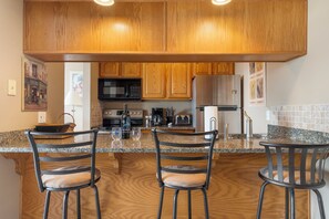 A kitchen with wooden cabinets, granite countertops, and a central island with bar stools. - Beautiful Lake View Condo, Newly Updated & Ideally Located (Branson)