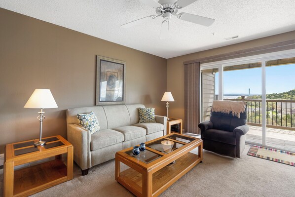 A living room with a sofa, two side tables with lamps, a coffee table, and a balcony with a view.