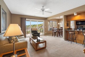 A spacious living area with a sofa, coffee table, and a dining table with chairs. There is a kitchen area with a microwave and bar stools.