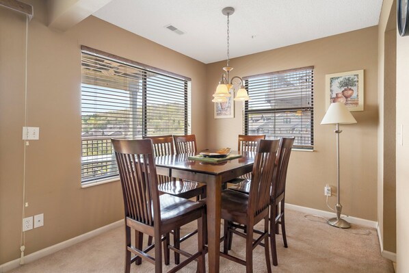 A dining area with a rectangular table surrounded by six wooden chairs, two pendant lights above, and a floor lamp to the side.