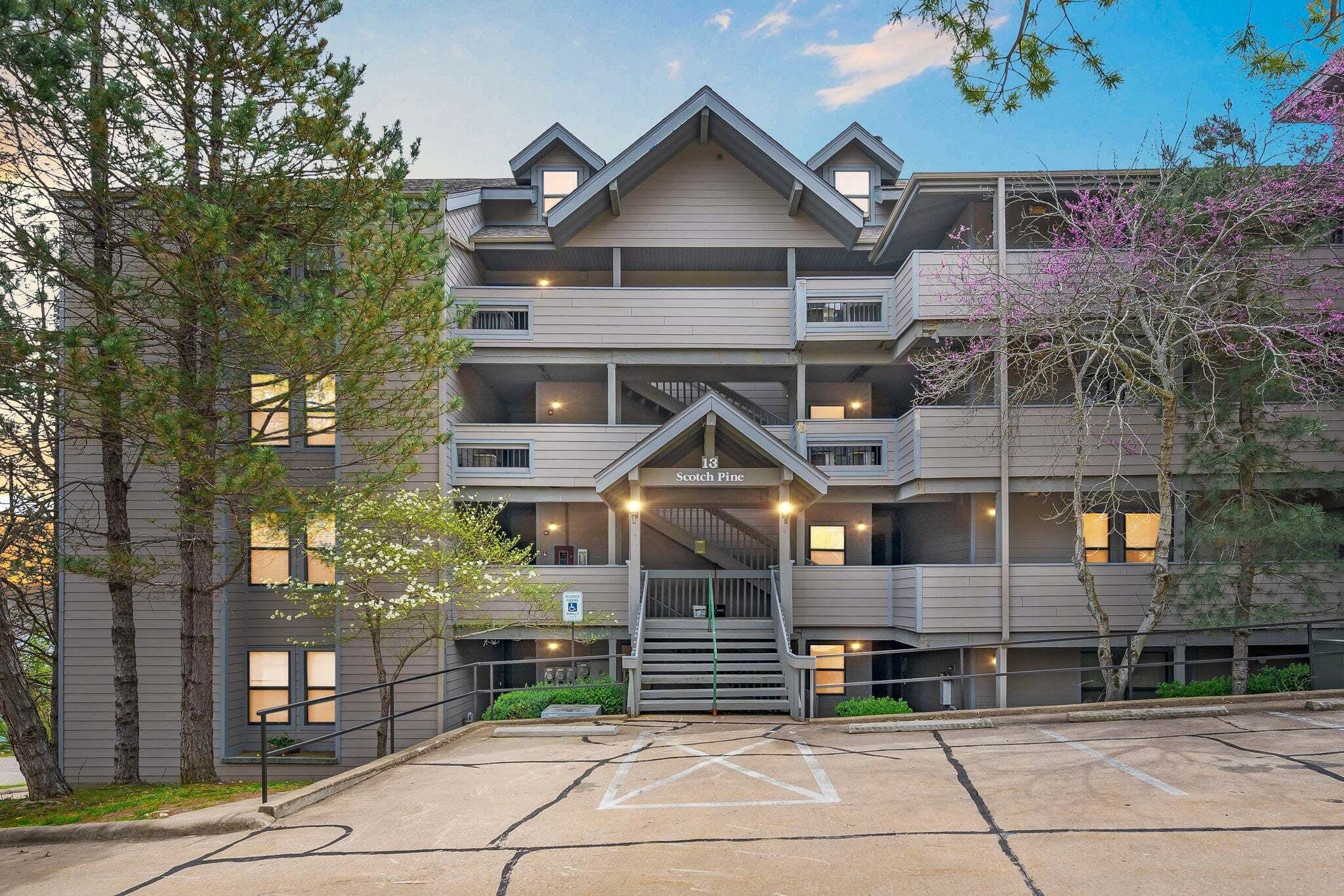 A multi-story building with a central entrance, balconies, and a parking area.