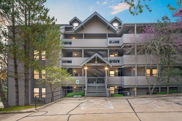 A multi-story building with a central entrance, balconies, and a parking area.
