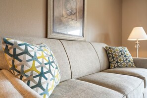 A beige sofa with patterned cushions and a framed artwork on the wall.