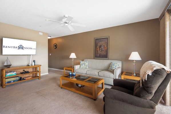 A living room with a sofa, armchair, coffee table, and a TV screen displaying a logo. - Beautiful Lake View Condo, Newly Updated & Ideally Located (Branson)
