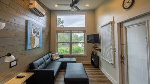 A modern living room with a sectional sofa, a flat-screen TV, and a large window offering a view of greenery. - Time Flies on the River (Bryson City)