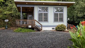 A small, single-story cabin with a porch, surrounded by dense forest. - Time Flies on the River (Bryson City)