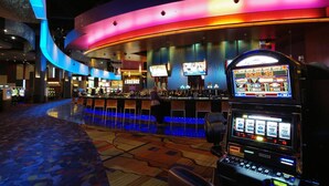 A casino with a curved bar area, slot machines, and a large screen displaying a game. - Time Flies on the River (Bryson City)