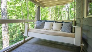 A wooden porch with a bench and cushions, surrounded by trees. - Charming Mountain Cabin Near Boone (Boone)