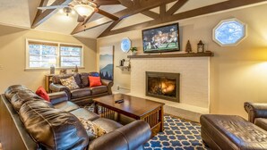 A cozy living room with a fireplace, leather sofas, a television, and a ceiling fan. - Charming Mountain Cabin Near Boone (Boone)