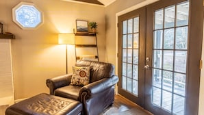 A leather armchair with a cushion, a small table with a lamp, and a large window with a view of trees. - Charming Mountain Cabin Near Boone (Boone)