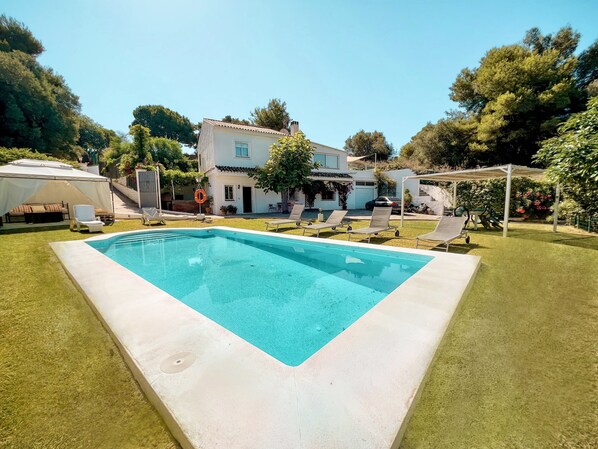 Relax by the pool surrounded by lush greenery and a well-manicured lawn.