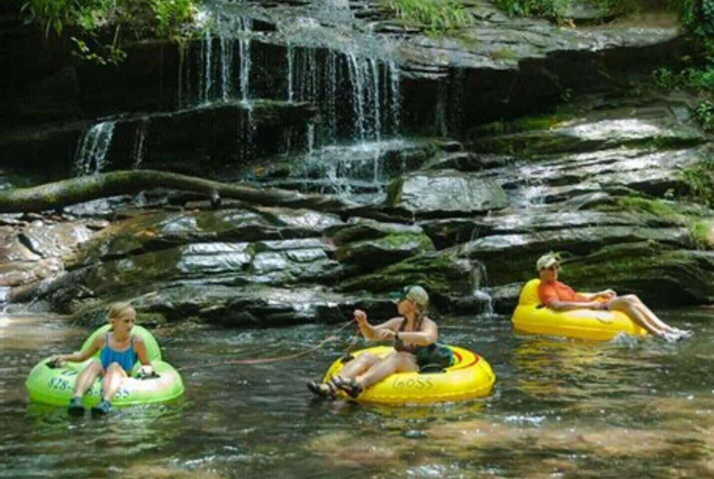 Three people on inflatable tubes in a natural water setting with a waterfall.