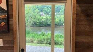 A wooden door with a 'WELCOME' sign above it, leading to a deck with a view of a river and greenery. - Ship Shak on the River (Bryson City)