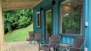 A covered outdoor area with a wooden deck, two wicker chairs, and a table. - Ship Shak on the River (Bryson City)