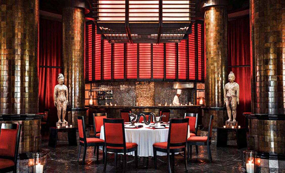Un restaurant doté d’une grande table ronde au centre, de chaises rouges et de statues décoratives.