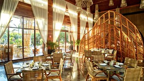 Un comedor interior con mobiliario de mimbre, ventanas amplias y lámparas colgantes.