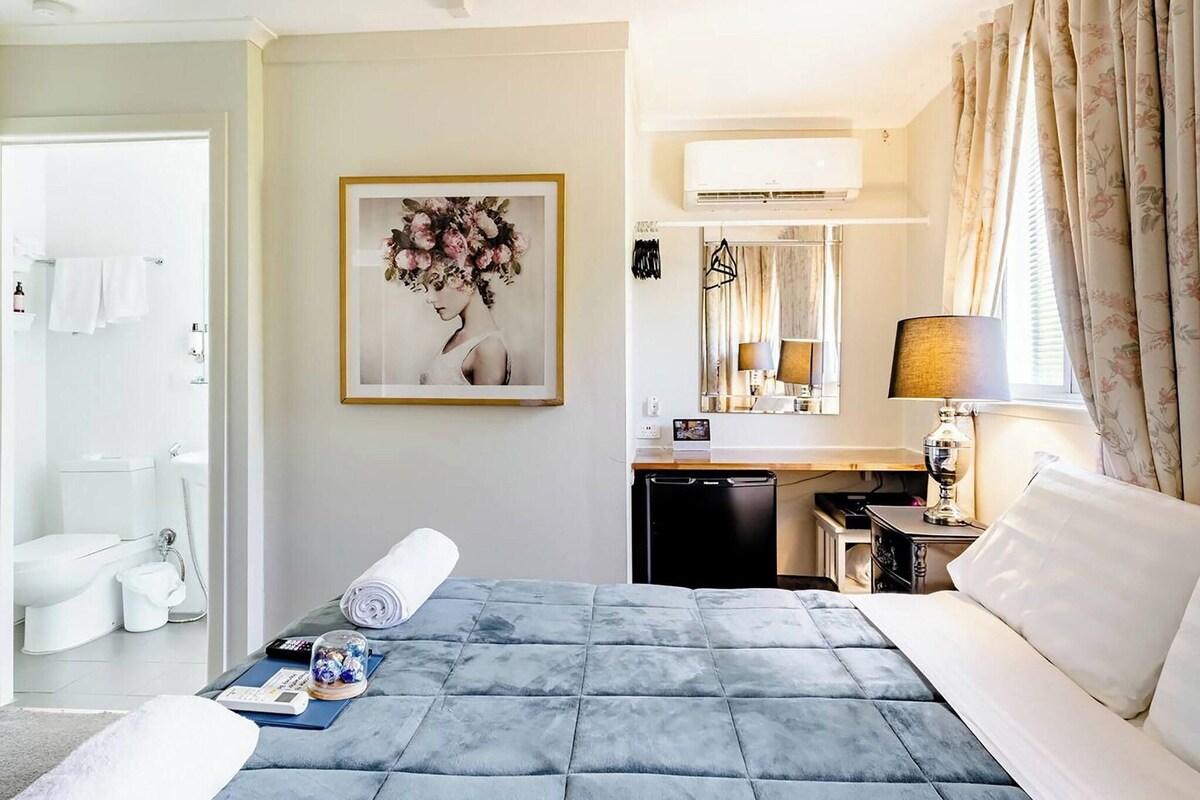 A hotel room with a bed, a desk, a bathroom, and a large window with curtains.