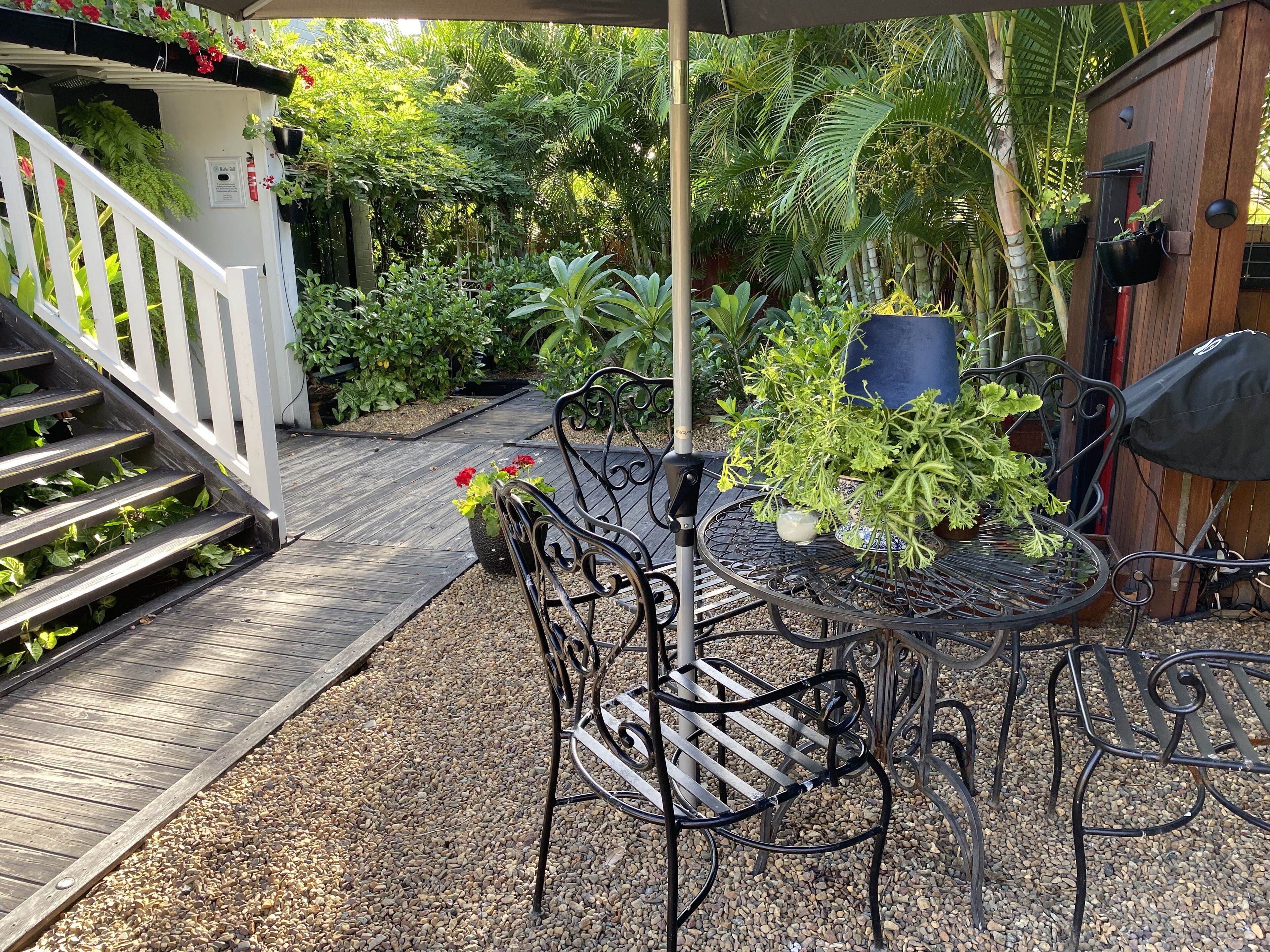 A patio with a metal table and chairs, surrounded by potted plants and a wooden deck.