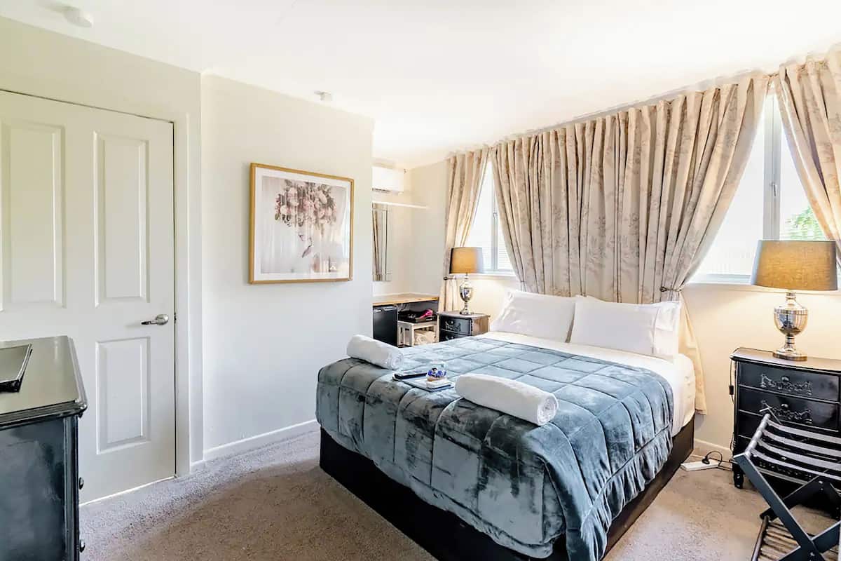 A neatly arranged hotel room with a bed, bedside tables, a desk, and a chair.