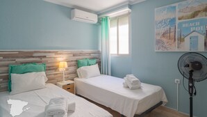 A hotel room with two beds, a nightstand, a wall-mounted air conditioner, a standing fan, and a beach-themed wall decoration. - CostaBlancaDreams - Nineteen / Frentemar in Calpe (Calpe)