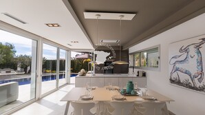 A modern kitchen with a large island, a dining area with a table set for four, and a large window overlooking a swimming pool. - CostaBlancaDreams - Villa Gran Sol en Calpe (Calpe)