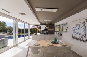 Une cuisine moderne dotée d’un grand îlot central, d’un coin repas avec une table pour quatre personnes et d’une grande fenêtre donnant sur une piscine.