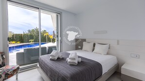 A modern hotel room with a large bed, a view of a swimming pool, and a sliding glass door leading to an outdoor area. - CostaBlancaDreams - Villa Gran Sol en Calpe (Calpe)