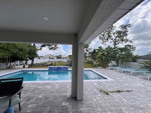 A covered outdoor swimming pool area with lounge chairs and a view of a residential neighborhood. - Beautiful 4 Bedroom house 25 mins away from the beach (Cape Coral)