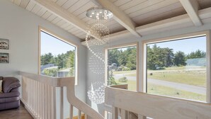 A wooden staircase with a railing, large windows with a view of a green landscape, and a hanging light fixture. - Sea Ranch Ocean Views 4 bedrooms + office (Sea Ranch)