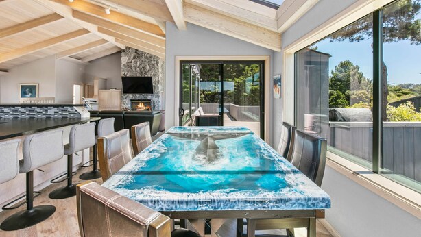 A modern kitchen with a bar area, a dining table with a unique blue tablecloth, and a large window offering a view of the outdoors. - Sea Ranch Ocean Views 4 bedrooms + office (Sea Ranch)