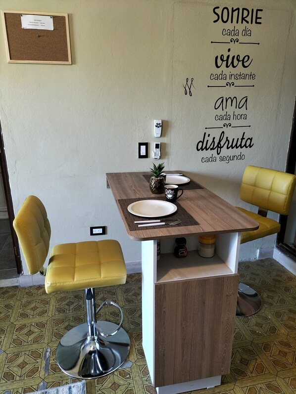 A small dining area with a wooden table, two yellow chairs, and a wall-mounted phone.