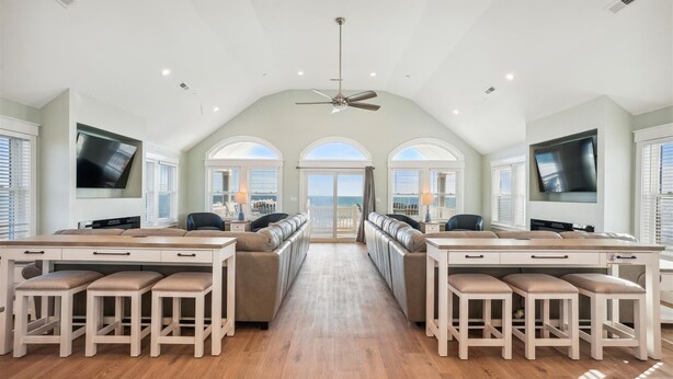 A spacious living area with a high ceiling, a ceiling fan, and a large TV on the wall. - 5373 - Wench's Pad 4 - Luxury Oceanfront Retreat | Sleeps 40 (Kill Devil Hills)