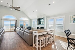Relax in this spacious living area with a high ceiling, featuring a curved sofa, dining table, and ocean views.
