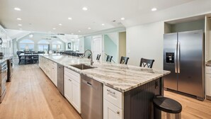 A spacious kitchen with a large island, stainless steel appliances, and a view to the outside. - 5373 - Wench's Pad 4 - Luxury Oceanfront Retreat | Sleeps 40 (Kill Devil Hills)