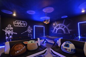 Habitación temática de Star Wars con mesa de billar, sofás y cojines con motivos de Star Wars, y un letrero de neón.