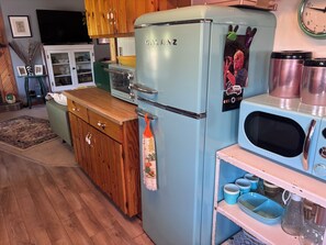 Une cuisine d’époque avec un réfrigérateur bleu, des armoires en bois, un four à micro-ondes et une horloge murale.
