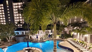 A nighttime pool area with lounge chairs, a pool, and palm trees. - Enjoy a Poolside Luxury Condo and dock, & only a 3 min walk to Vanderbilt Beach. (Naples)