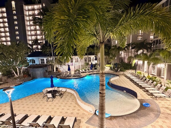 A nighttime pool area with lounge chairs, a pool, and palm trees. - Enjoy a Poolside Luxury Condo and dock, & only a 3 min walk to Vanderbilt Beach. (Naples)