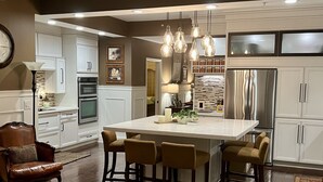 A modern kitchen with white cabinetry, a central island with bar stools, and pendant lighting. - Enjoy a Poolside Luxury Condo and dock, & only a 3 min walk to Vanderbilt Beach. (Naples)