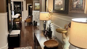 A hallway with a wooden bench, a lamp, and a decorative figure. There are framed pictures on the wall and a chandelier. - Enjoy a Poolside Luxury Condo and dock, & only a 3 min walk to Vanderbilt Beach. (Naples)
