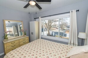 Un dormitorio con cama, cómoda, espejo, ventana y ventilador de techo.