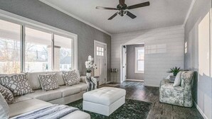 Ein Wohnzimmer mit Sofa, Hocker und Sessel, einem Deckenventilator und Blick durch ein Fenster.