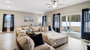 A spacious living room with a large sectional sofa, a ceiling fan, and a sliding glass door leading to an outdoor area.