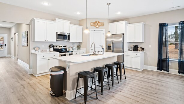 A modern kitchen with white cabinetry, a central island with bar stools, stainless steel appliances, and pendant lighting.
