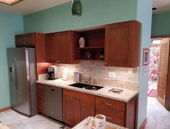 A kitchen with wooden cabinets, a stainless steel refrigerator, a coffee maker, and a sink. - POIPU BEACH HOME, Kauai's famous sunny south shore. (Koloa)